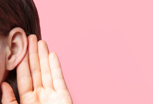 The girl listens attentively with her palm to her ear close-up on a pink background
